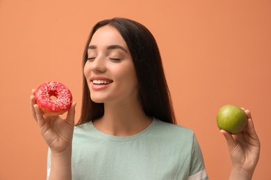 Woman choosing between apple and doughnut on orange background