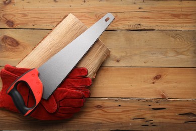 Photo of Saw with colorful handle and gloves on wooden background, top view. Space for text