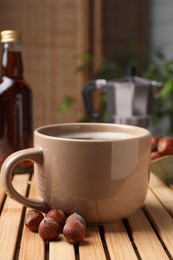 Photo of Mug of aromatic coffee with hazelnut syrup on wooden table, closeup