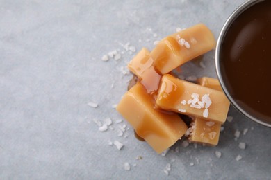 Photo of Yummy caramel candies, sauce and sea salt on grey table, top view. Space for text