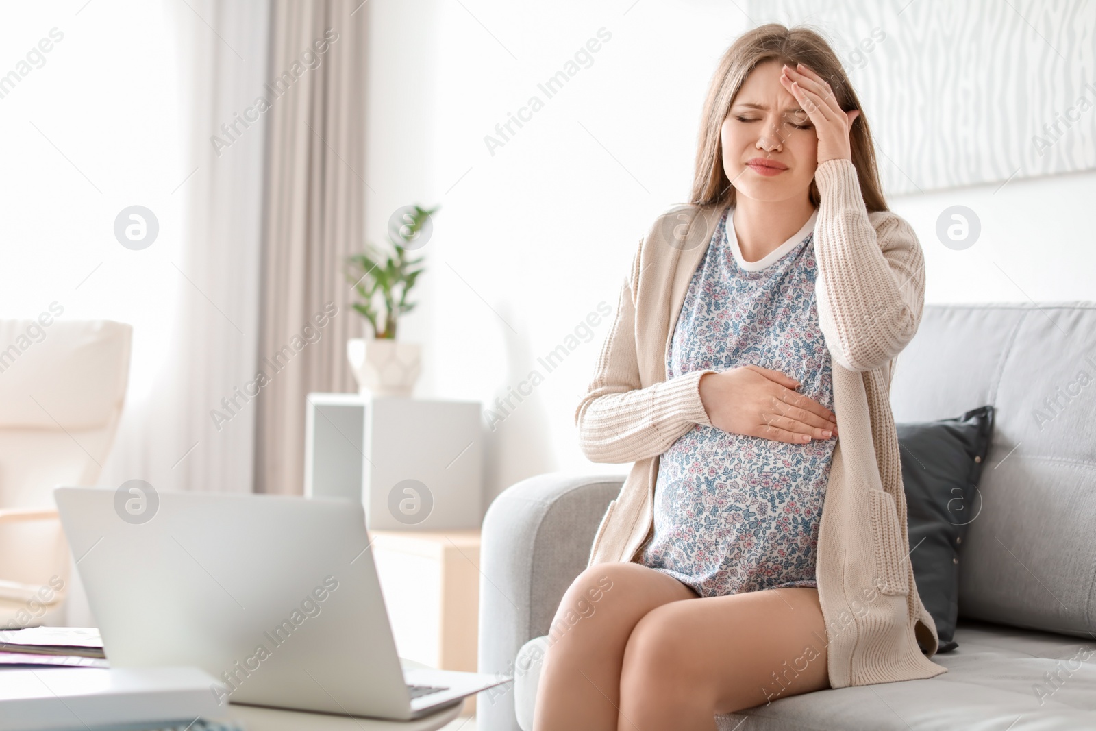 Photo of Young pregnant woman suffering from headache at home