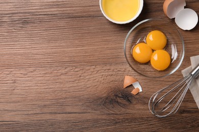 Photo of Bowls with raw egg yolks and white on wooden table, flat lay. Space for text