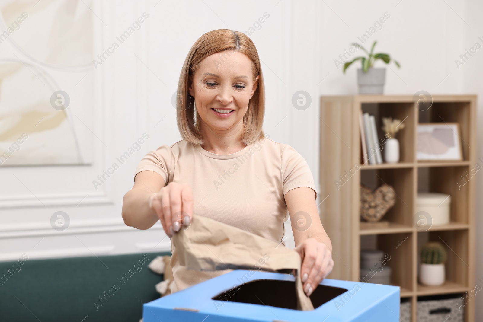 Photo of Garbage sorting. Smiling woman throwing crumpled paper into cardboard box in room