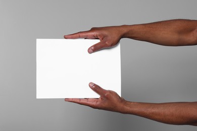 Photo of African American man holding sheet of paper on grey background, closeup. Mockup for design