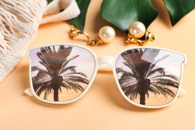 Image of Elegant sunglasses and beautiful earrings on beige background, closeup. Sky and palm tree reflecting in lenses