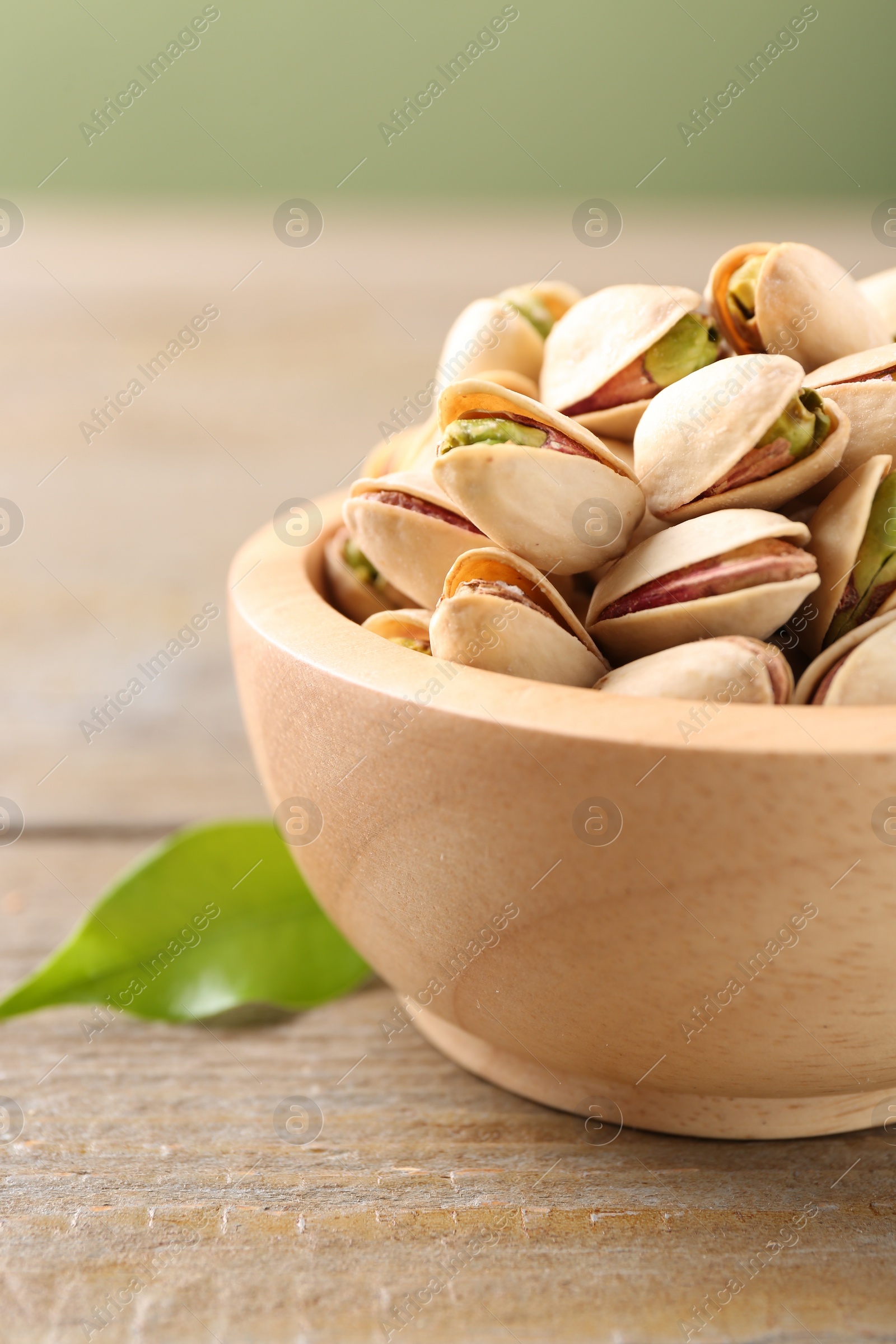 Photo of Tasty pistachios in bowl on wooden table, closeup