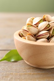 Photo of Tasty pistachios in bowl on wooden table, closeup