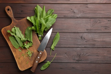 Fresh green sorrel leaves and knife on brown wooden table, flat lay. Space for text