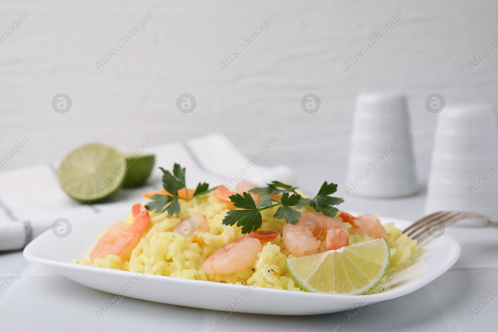 Photo of Delicious risotto with shrimps, lime and parsley on white table, closeup