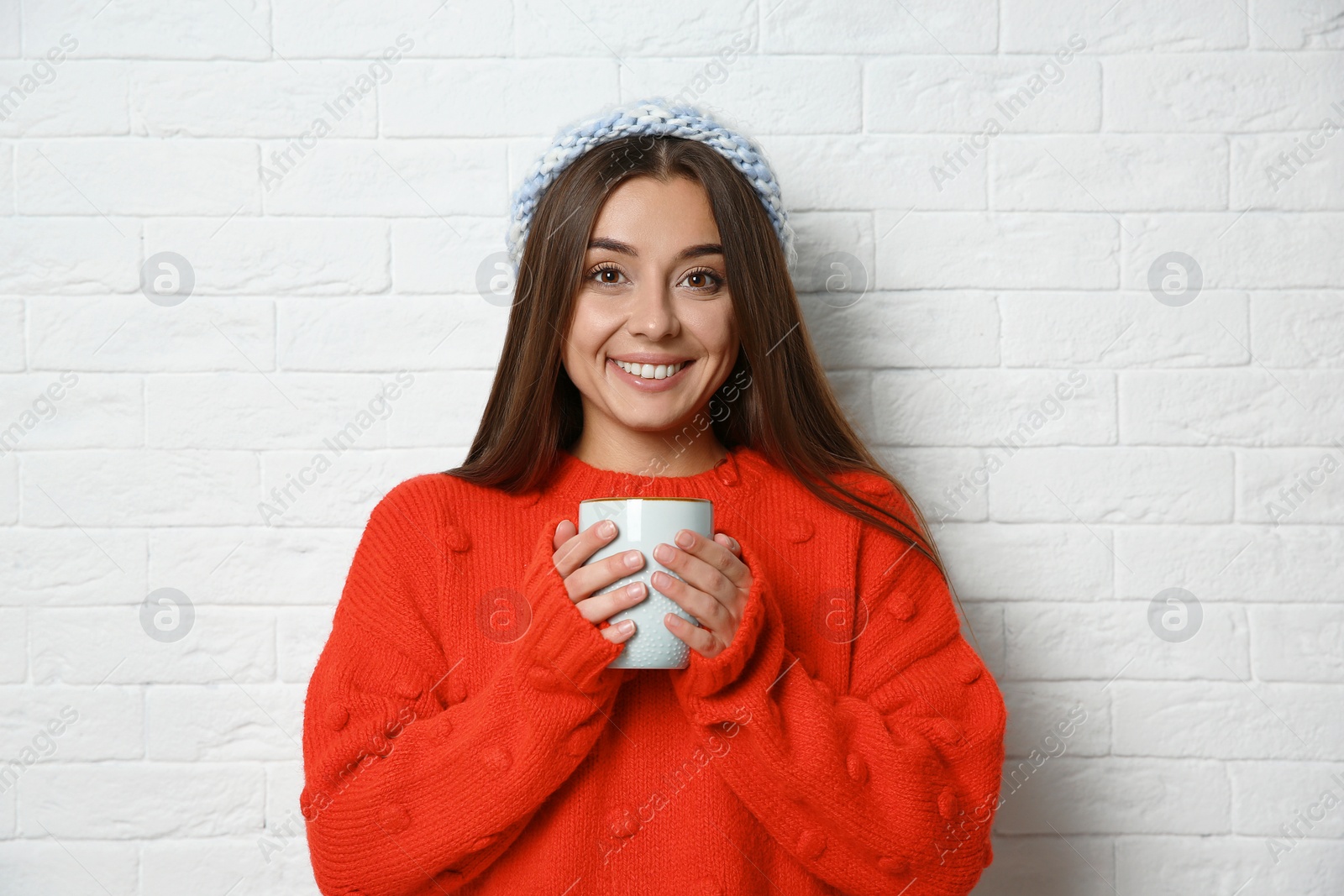 Photo of Beautiful young woman in warm sweater with cup of hot drink near white brick wall