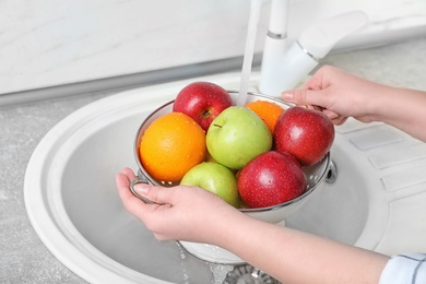 Photo of Woman washing fresh fruits in colander under water, closeup