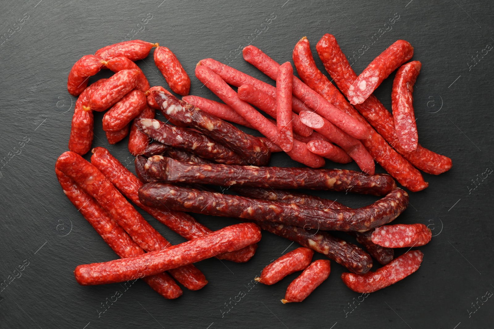 Photo of Different thin dry smoked sausages on black table, flat lay