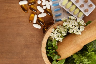 Photo of Mortar with fresh herbs and pills on wooden table, top view. Space for text