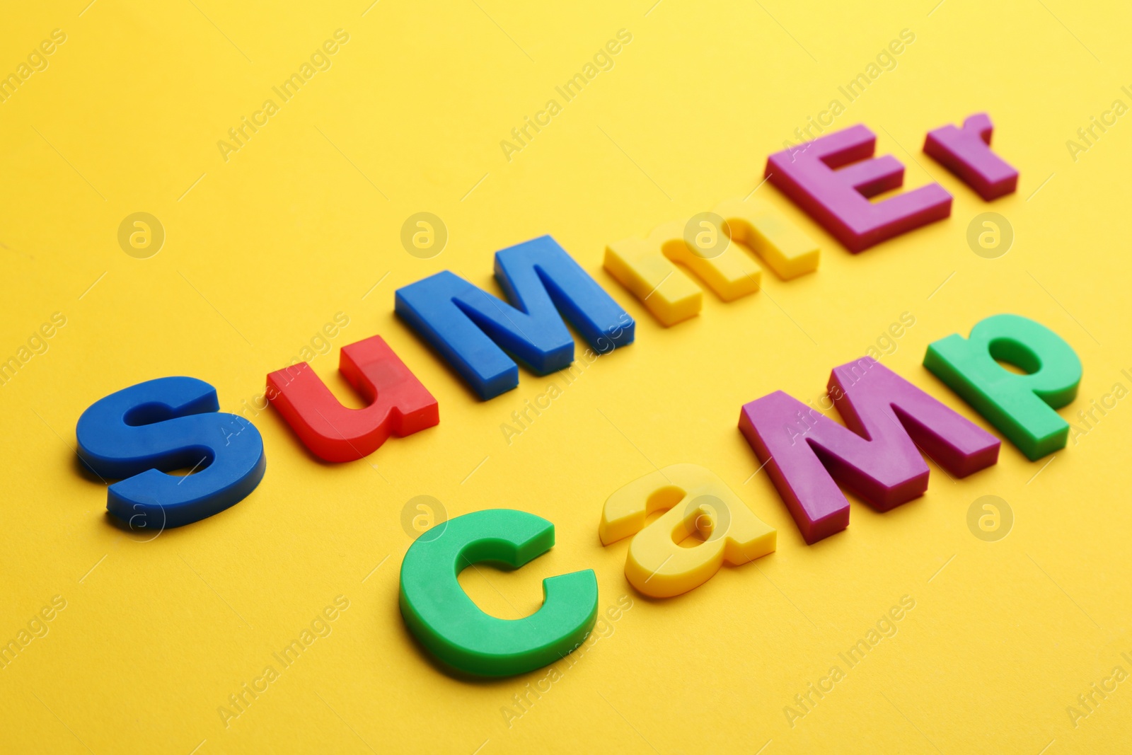 Photo of Phrase SUMMER CAMP made with magnet letters on yellow background, closeup