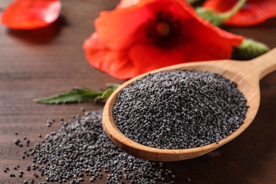 Spoon of poppy seeds and flower on wooden table, space for text
