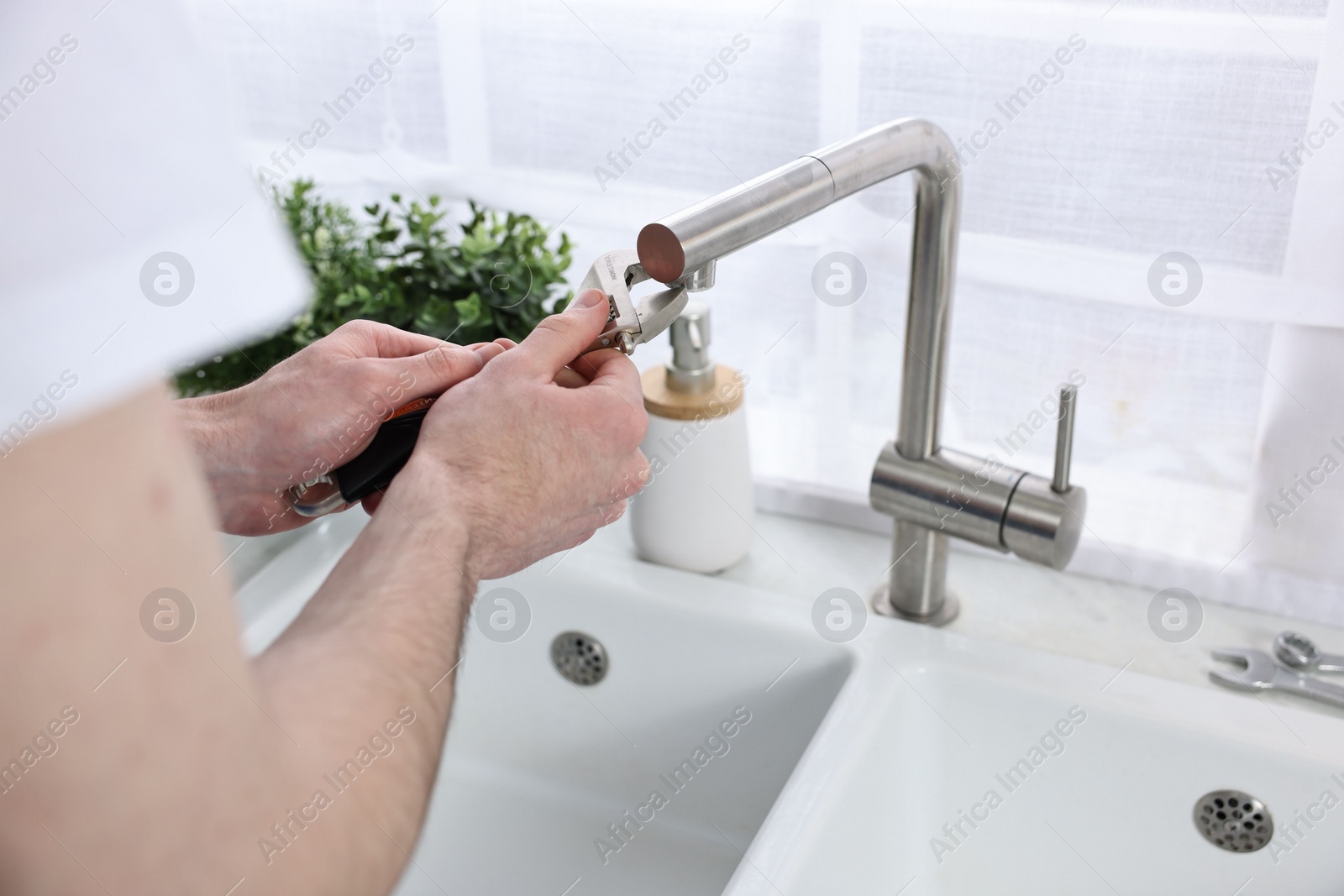 Photo of Plumber repairing faucet with spanner indoors, closeup