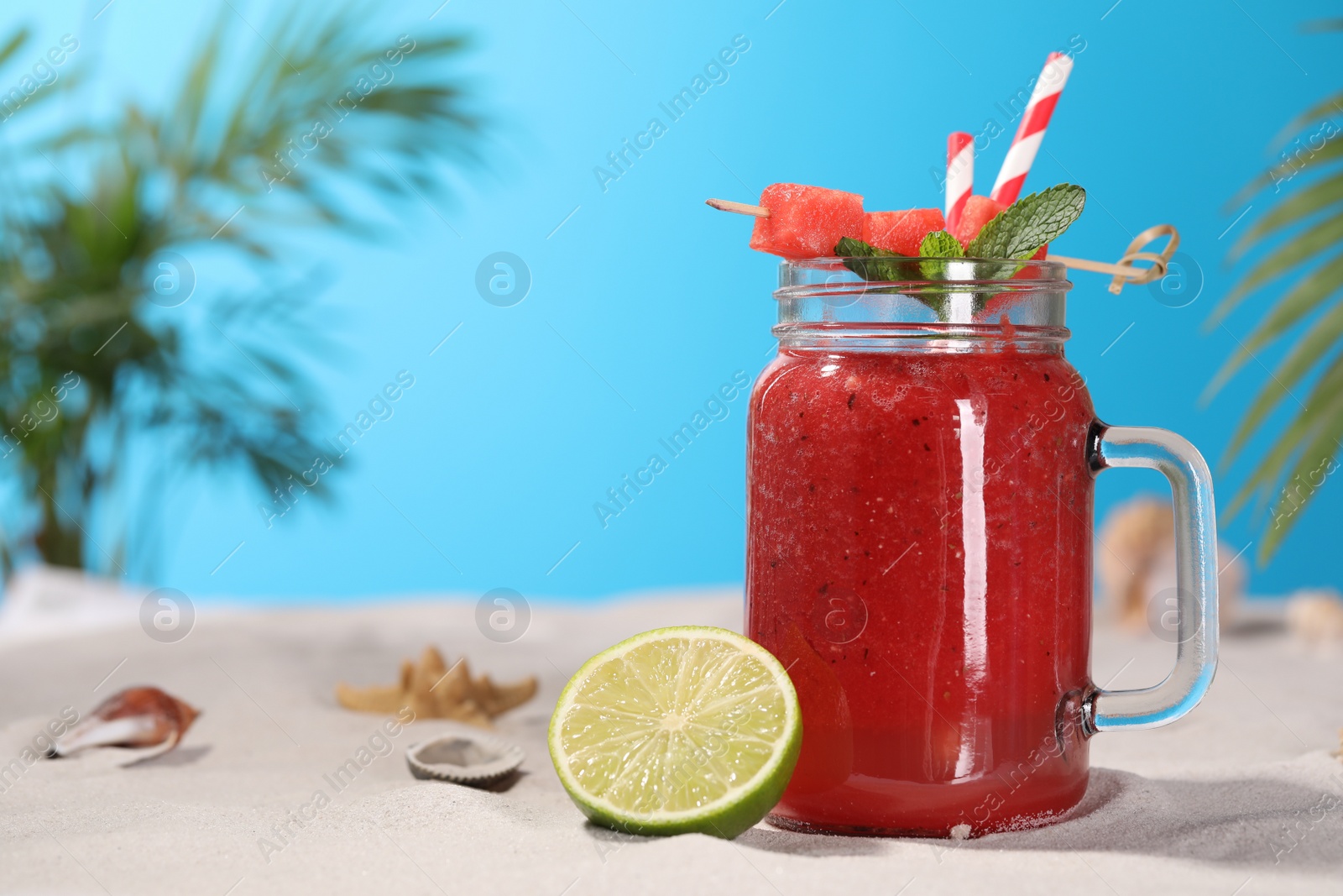 Photo of Tasty watermelon drink with lime in mason jar on sand, space for text