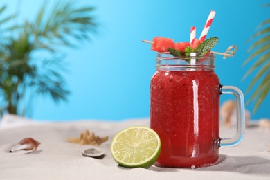 Tasty watermelon drink with lime in mason jar on sand, space for text