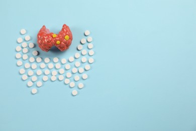 Photo of Endocrinology, Pills and model of thyroid gland on light blue background, flat lay. Space for text