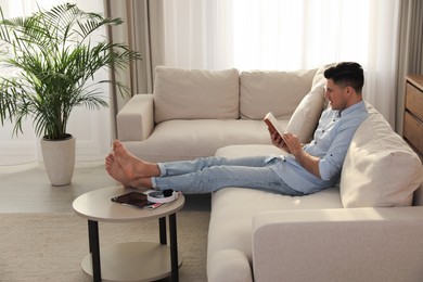 Man reading book on sofa in living room