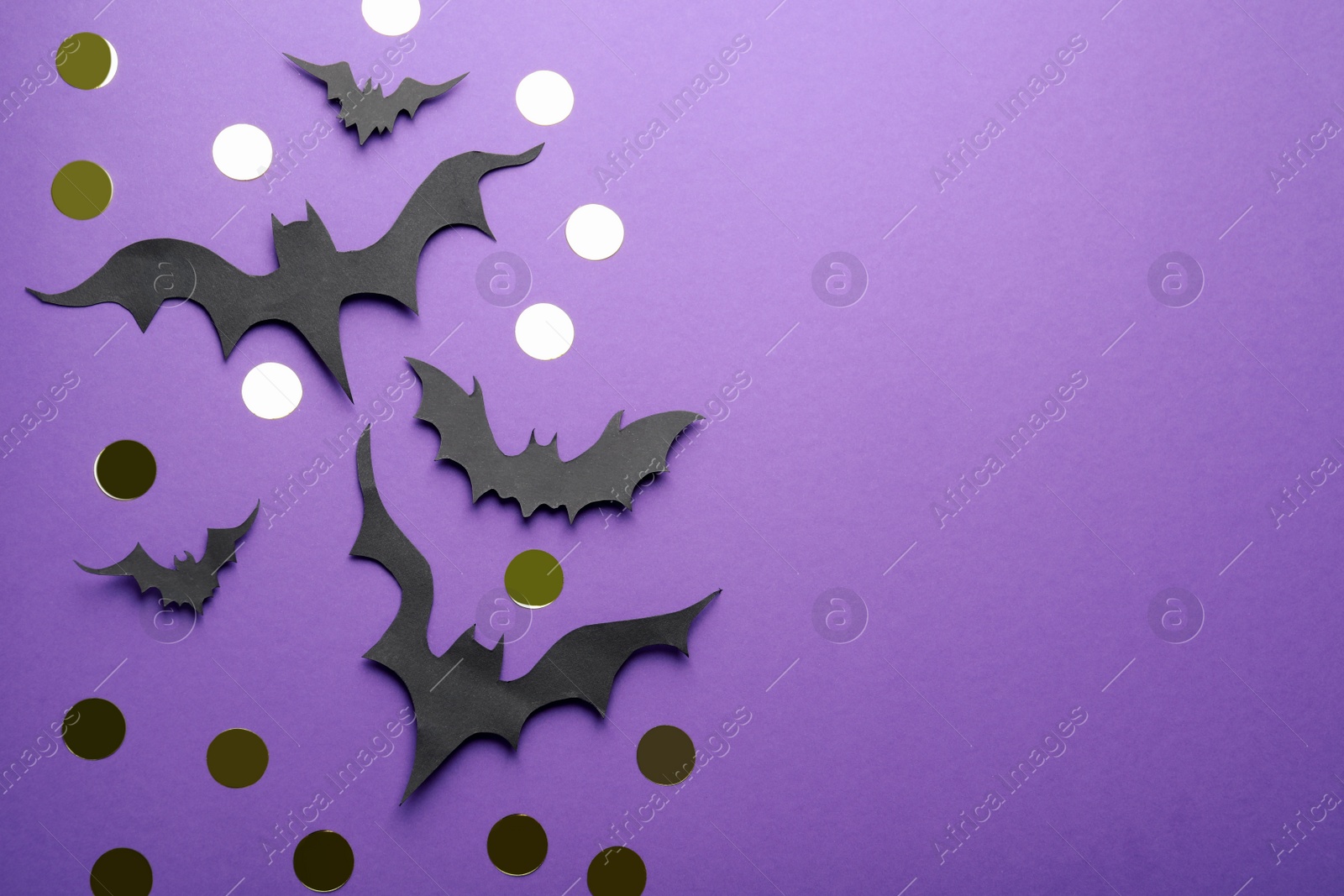 Photo of Flat lay composition with paper bats and golden confetti on purple background, space for text. Halloween decor