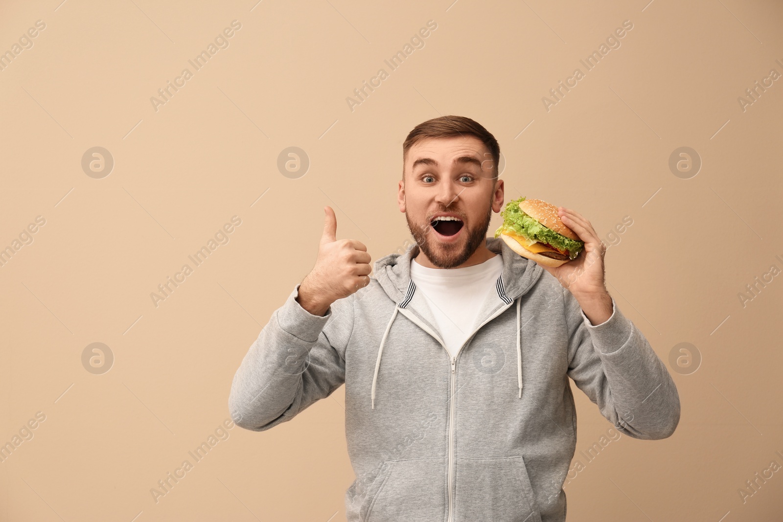 Photo of Young man eating tasty burger on color background. Space for text