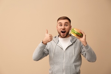 Photo of Young man eating tasty burger on color background. Space for text