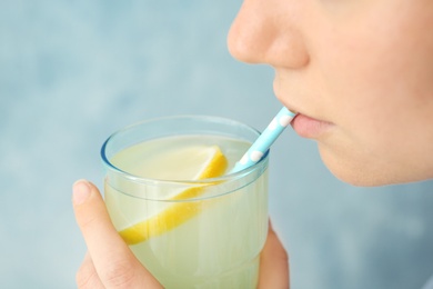 Young woman drinking lemon cocktail against color background