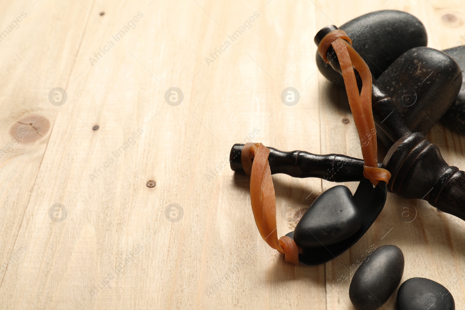 Photo of Black slingshot with stones on wooden table, closeup. Space for text