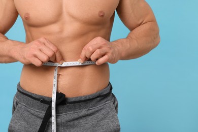Photo of Athletic man measuring waist with tape on light blue background, closeup. Weight loss concept