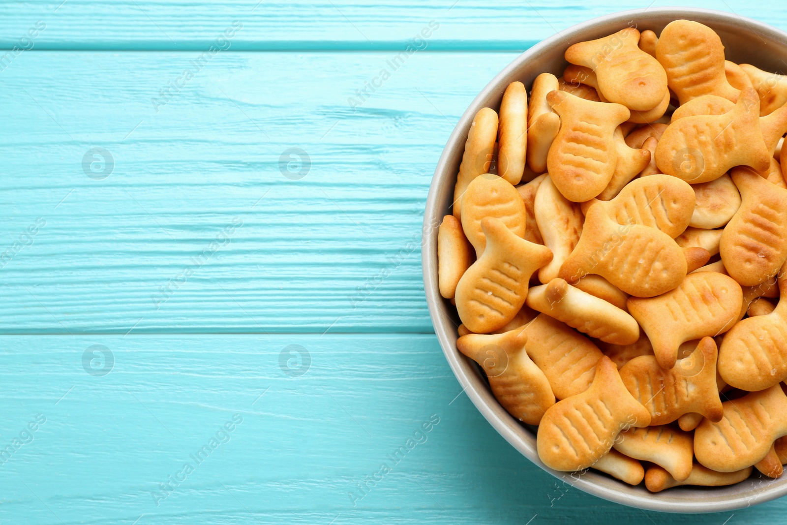 Photo of Delicious goldfish crackers in bowl on light blue wooden table, top view. Space for text