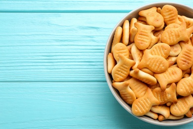 Photo of Delicious goldfish crackers in bowl on light blue wooden table, top view. Space for text