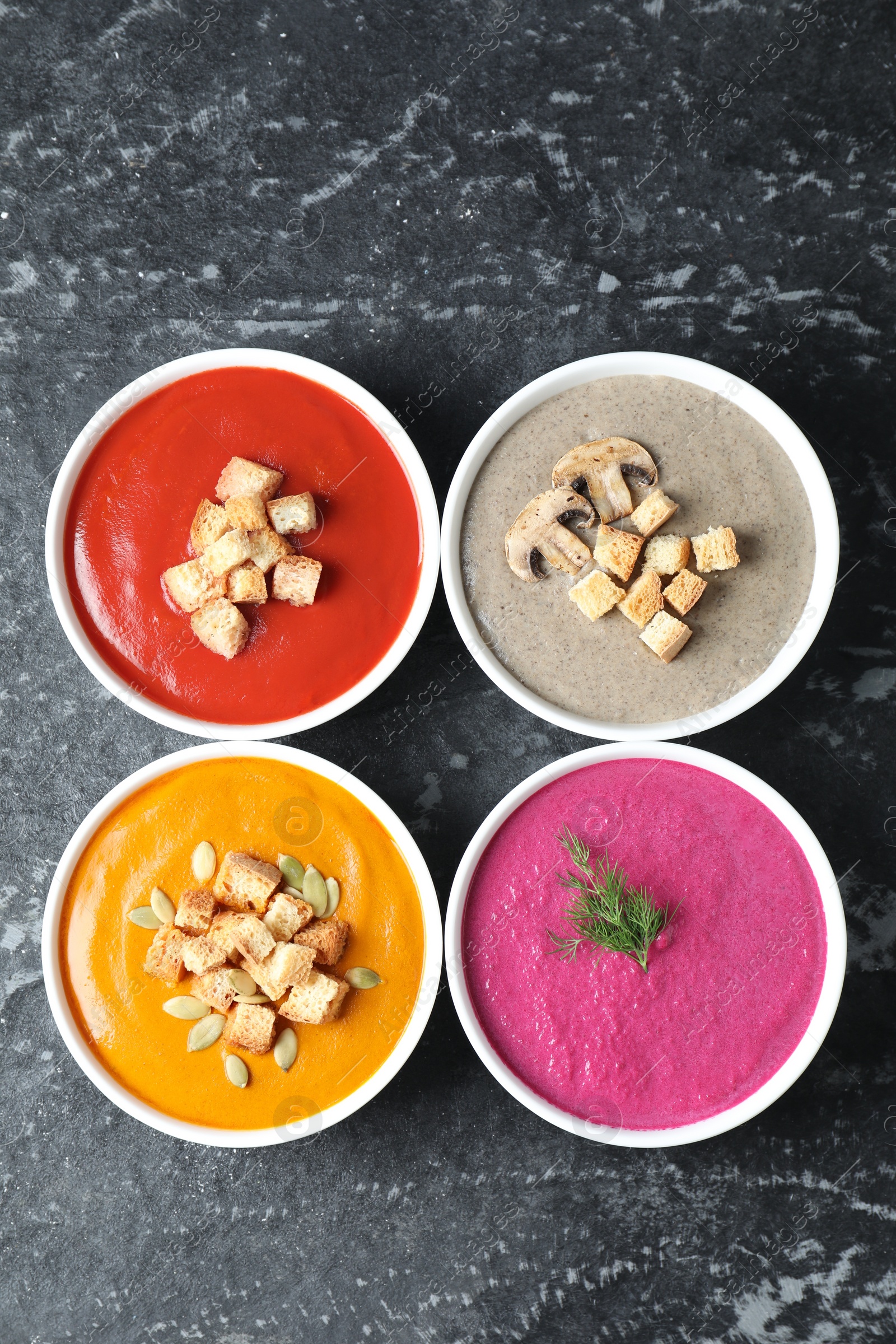 Photo of Different tasty cream soups in bowls on black textured table, flat lay