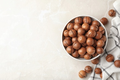 Photo of Bowl with organic Macadamia nuts and space for text on light background, top view