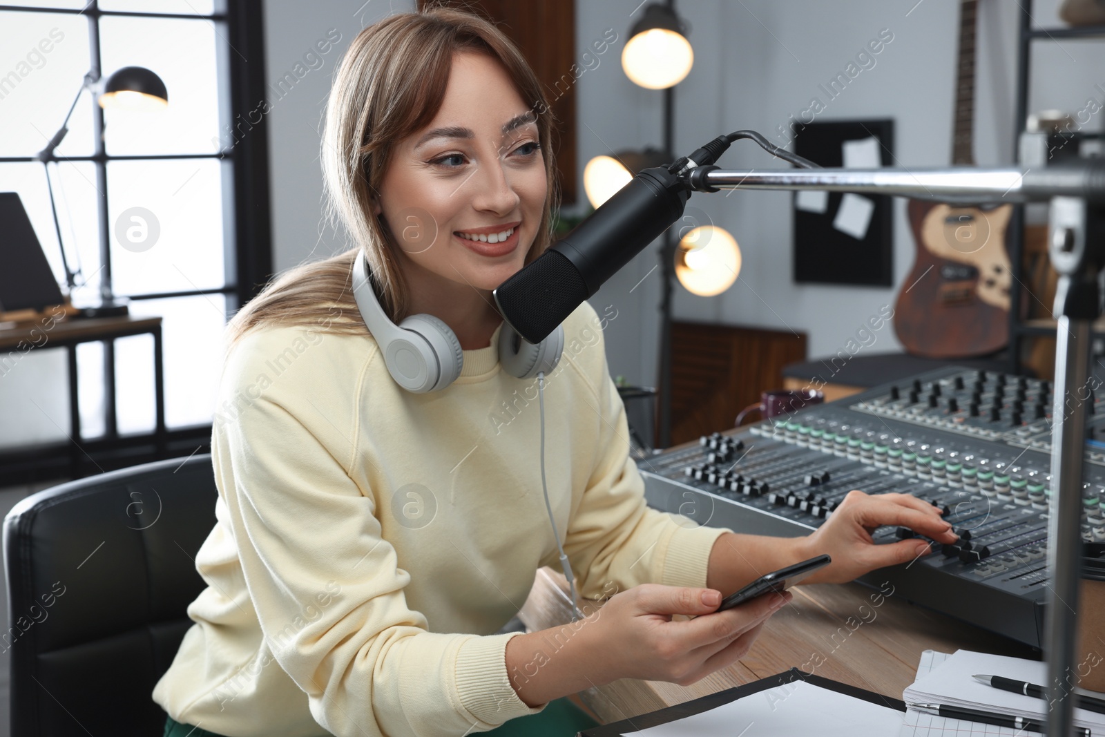 Photo of Woman with smartphone working as radio host in modern studio