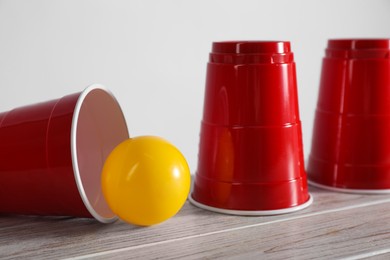 Photo of Shell game. Three red cups and ball on wooden table, closeup