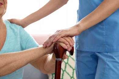 Photo of Nurse assisting elderly woman with cane, closeup