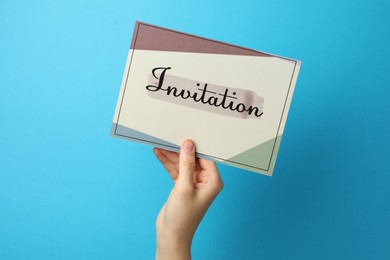 Woman holding beautiful card with word Invitation on light blue background, closeup