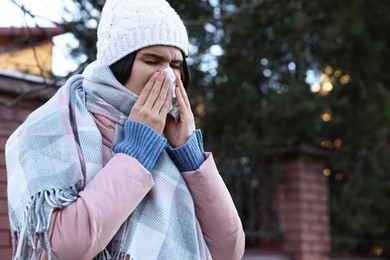 Photo of Woman with tissue blowing runny nose outdoors, space for text. Cold symptom