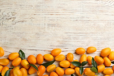 Photo of Fresh ripe kumquats on white wooden table, flat lay. Space for text