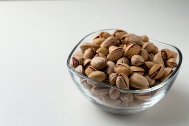 Photo of Bowl with pistachio nuts on white background, space for text