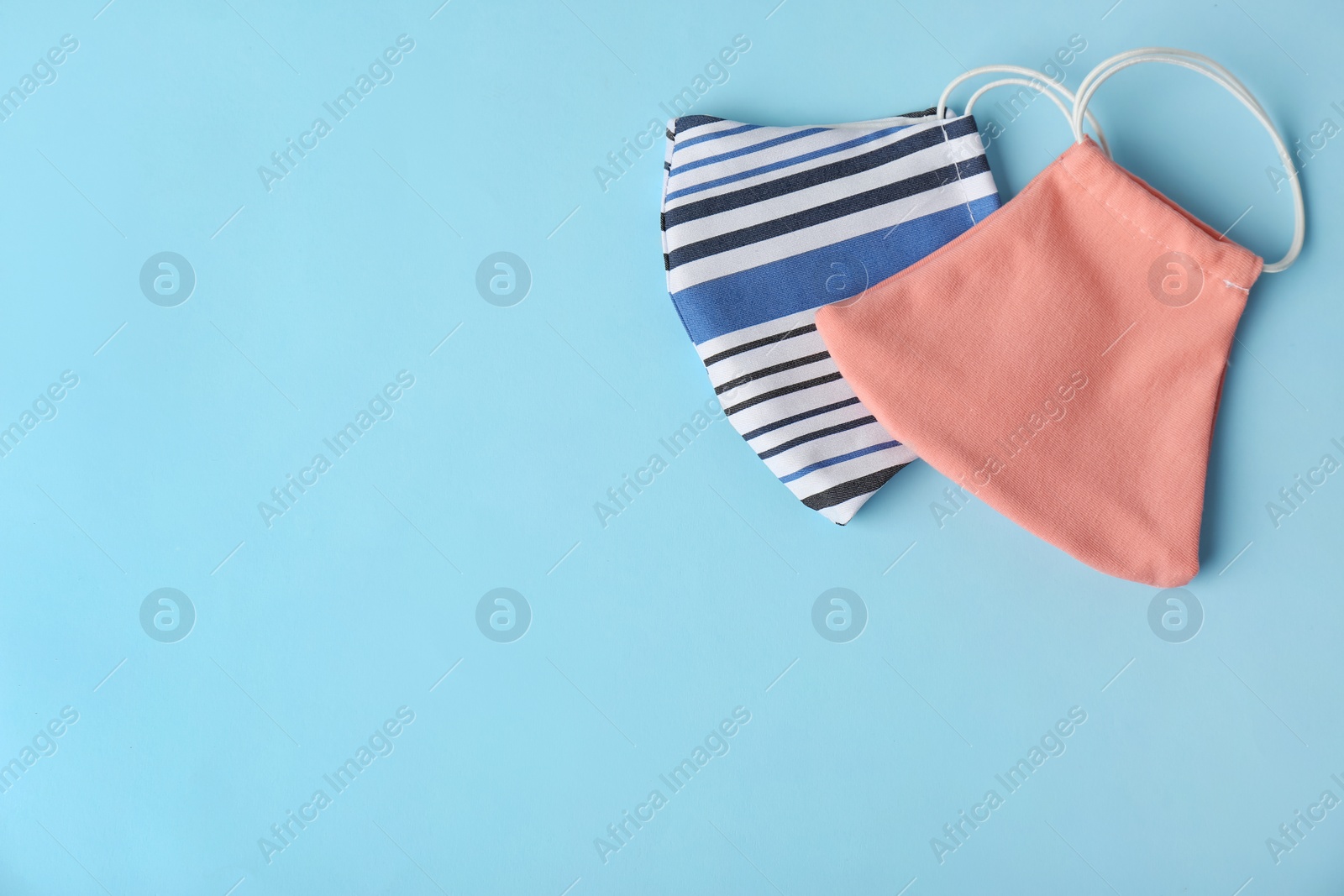 Photo of Homemade protective face masks on light blue background, flat lay. Space for text