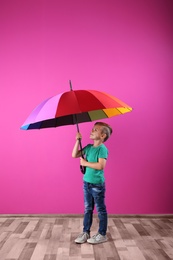 Little boy with rainbow umbrella near color wall