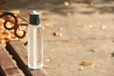 Sport bottle of water on wooden bench outdoors, space for text