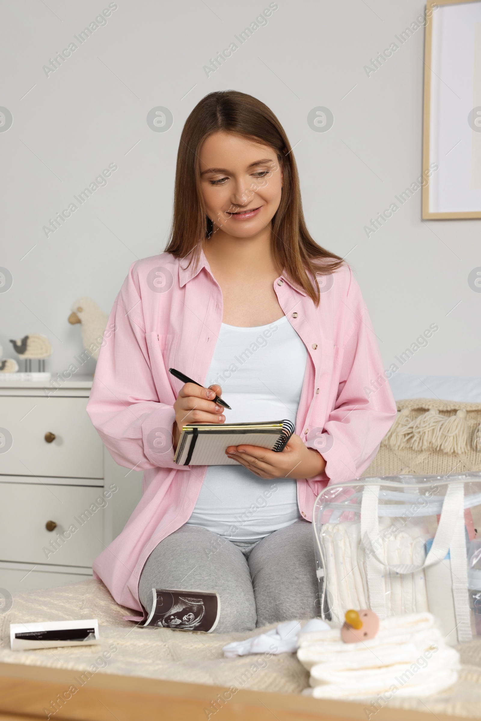 Photo of Pregnant woman preparing list of necessary items to bring into maternity hospital in bedroom