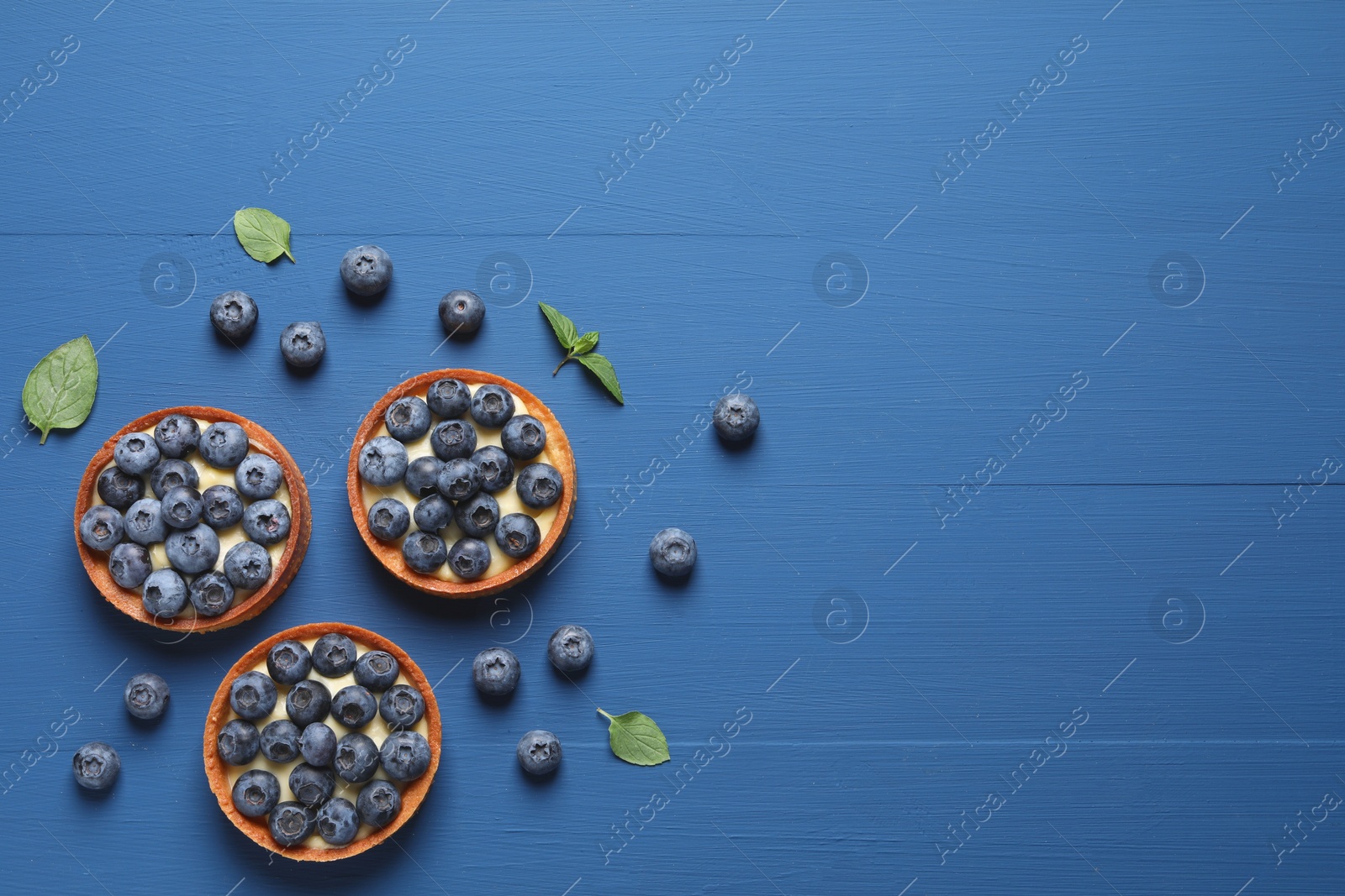 Photo of Tartlets with fresh blueberries on blue wooden table, flat lay and space for text. Delicious dessert