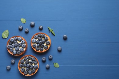 Photo of Tartlets with fresh blueberries on blue wooden table, flat lay and space for text. Delicious dessert