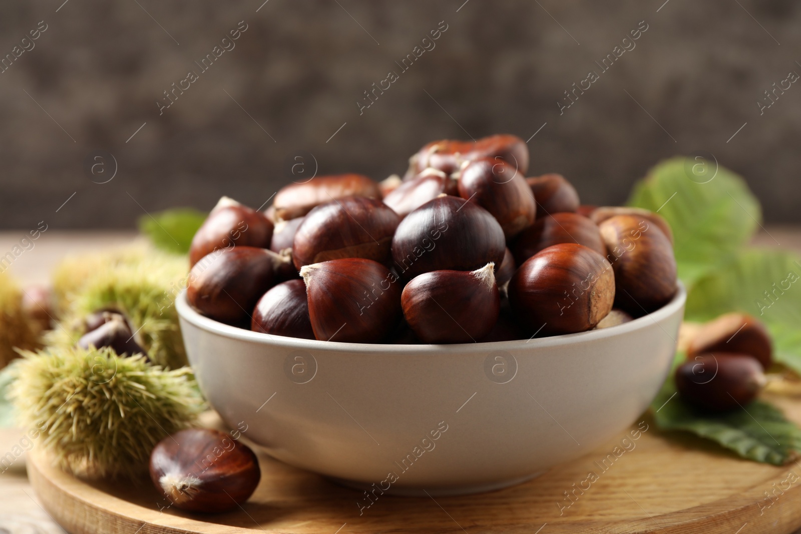 Photo of Fresh sweet edible chestnuts in bowl on wooden board