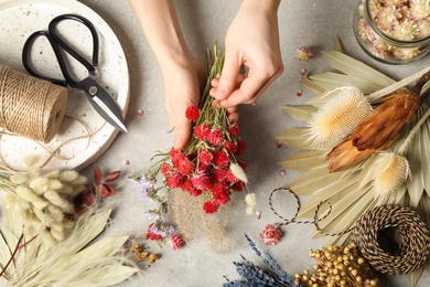 Florist making bouquet of dried flowers at light grey table, above view