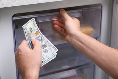 Photo of Man hiding money in refrigerator, closeup. Financial savings